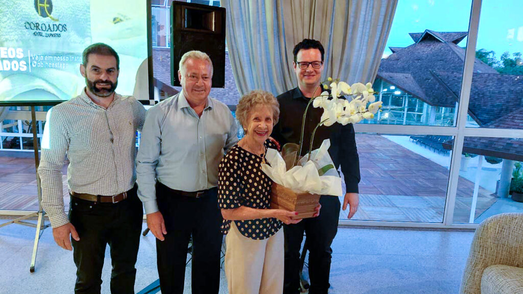 A elegância do reconhecimento: A diretoria da ABIH Regional Oeste, representada por Diego Vezaro, Carlos Silva e Richardson Voltolini, presta justa homenagem à Sra. Iraci Pissinin Sossella. A valorização de quem construiu nossa história é a marca desta gestão. 🥂 (Foto: Divulgação)